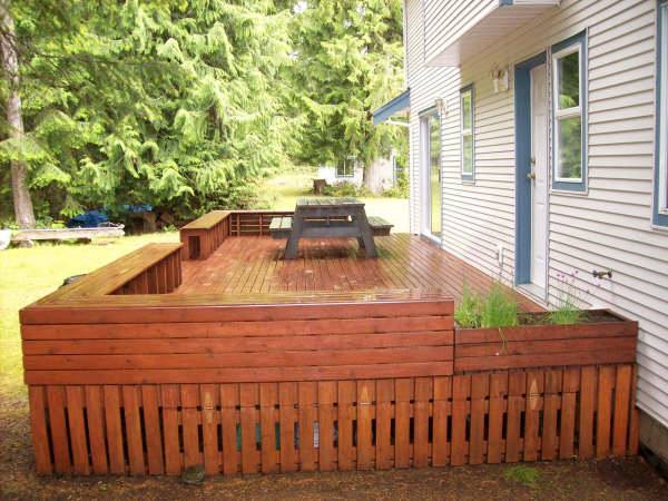 Photo of a backyard wood deck showing benches along sides and storage area underneath.